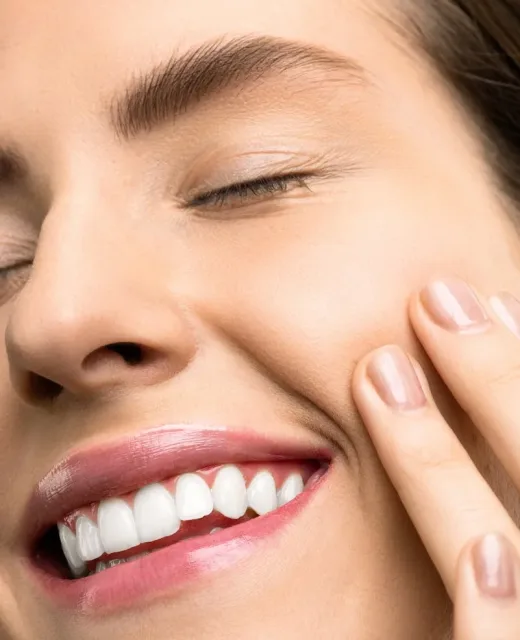 A close-up portrait of a joyful woman with closed eyes, pink lipstick, and her hand touching her cheek.